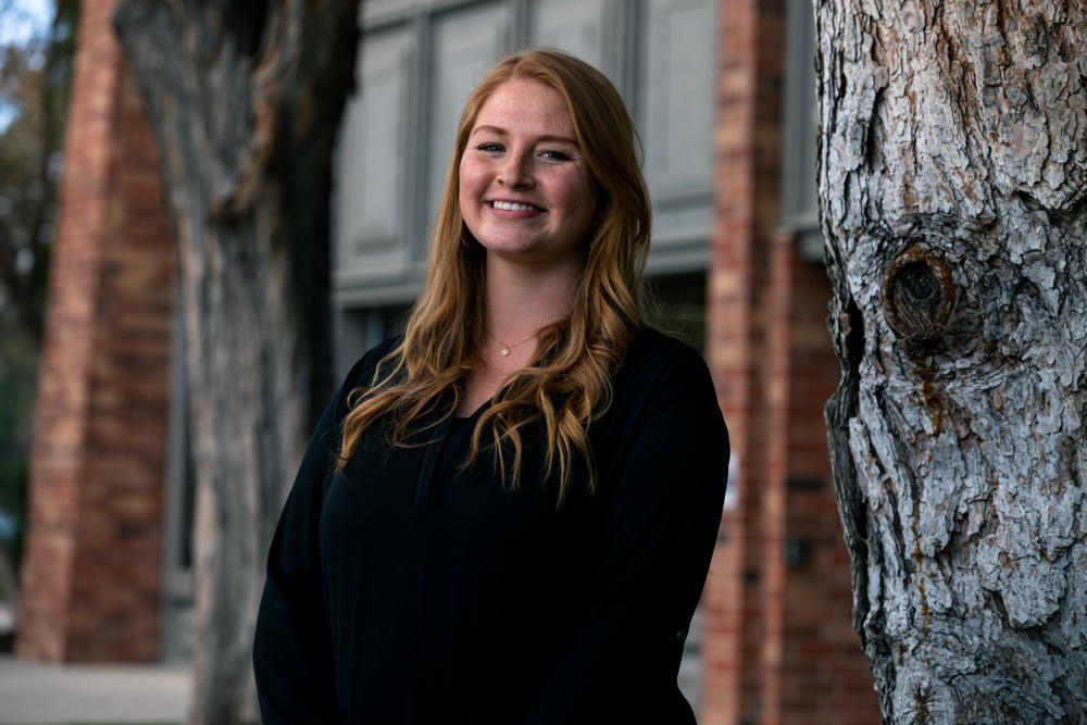 headshot photo of female with brick wall and trees in background